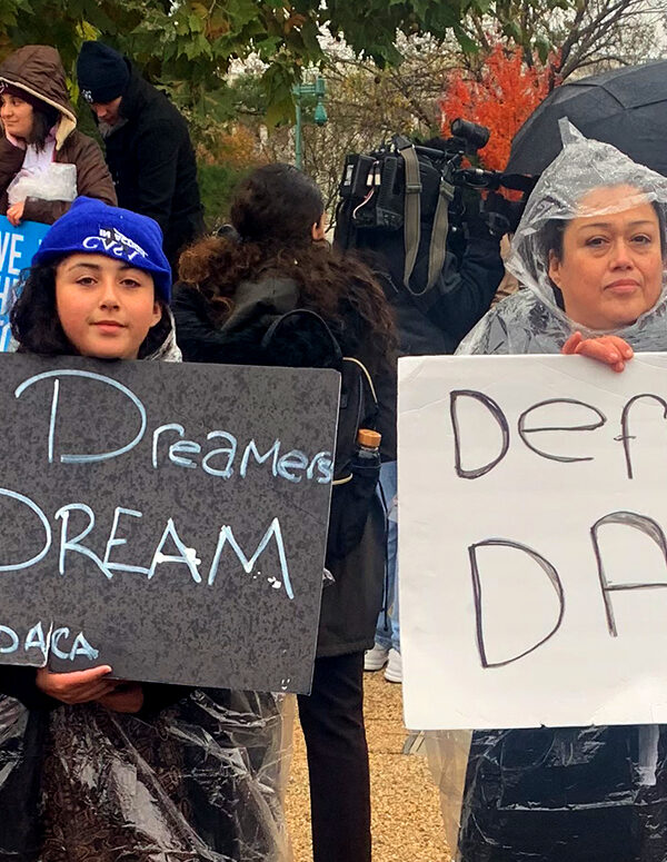 Two people at the Home is Here rally at the Supreme Court holding signs that say "Let Dreamers Dream" and "Defend DACA". In the background are two people holding ACLU signs that say "We the People".