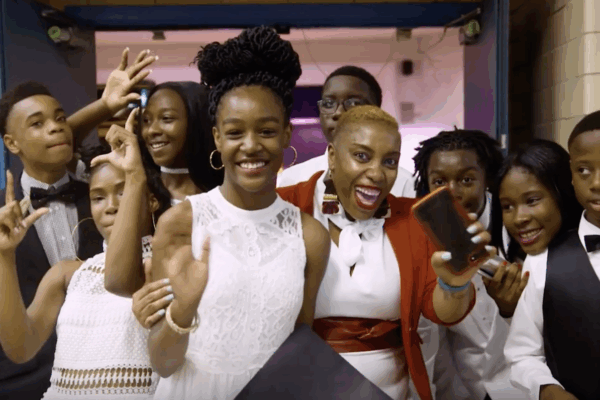 Shantay McKinily is pictured surrounded by about ten students at a formal school event. Studetns are wearing dresses and suits. Everyone is smiling.