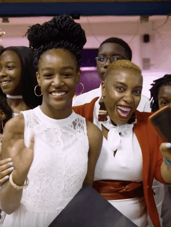 Shantay McKinily is pictured surrounded by about ten students at a formal school event. Studetns are wearing dresses and suits. Everyone is smiling.