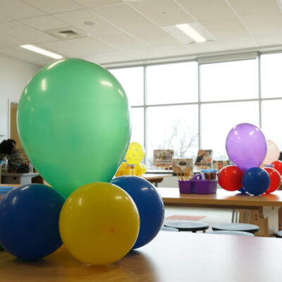 Art classroom at Bay-Brook Elementary Middle School in Baltimore, MD. There are colorful balloons on desks and lots of sunlight coming through the wall of windows.