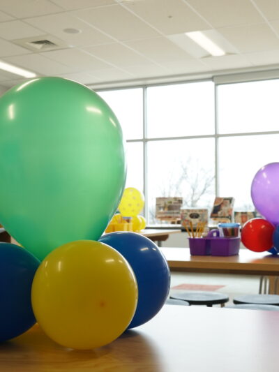 Art classroom at Bay-Brook Elementary Middle School in Baltimore, MD. There are colorful balloons on desks and lots of sunlight coming through the wall of windows.