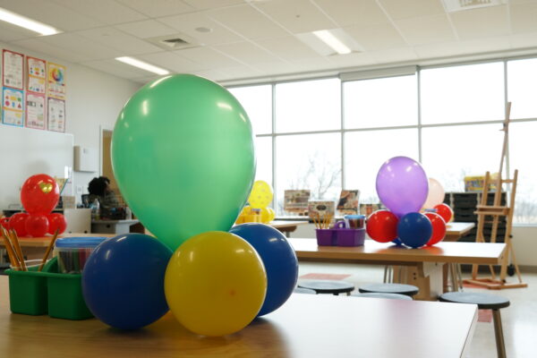 Art classroom at Bay-Brook Elementary Middle School in Baltimore, MD. There are colorful balloons on desks and lots of sunlight coming through the wall of windows.