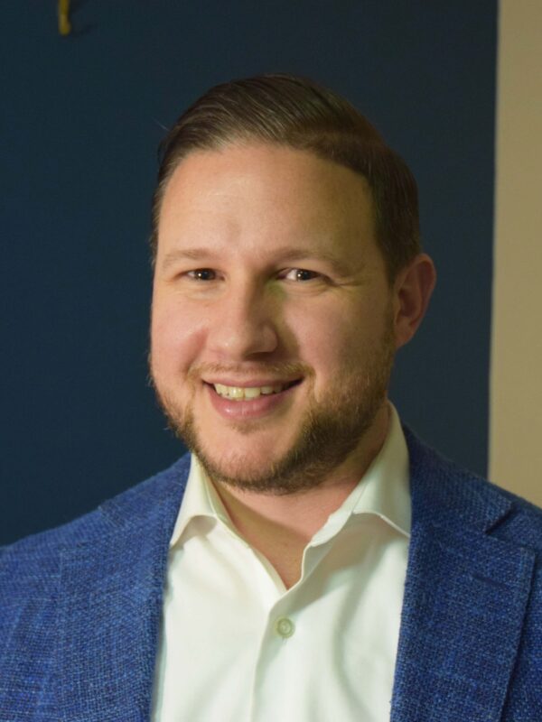 Eric Gillman, white man, wearing blue suit jacket, light yellow collared shirt