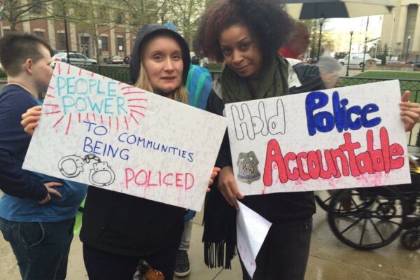 Two women at a rally with signs calling for "People Power to the Communities being Policed" and "Hold Police Accountable"