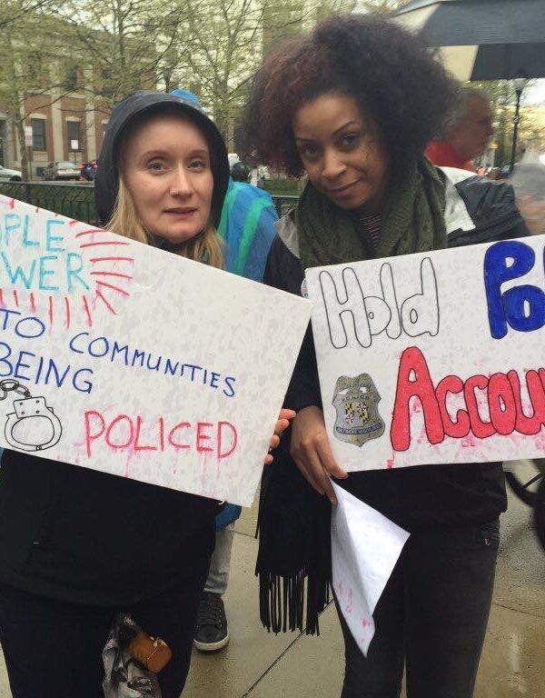 Two women at a rally with signs calling for "People Power to the Communities being Policed" and "Hold Police Accountable"
