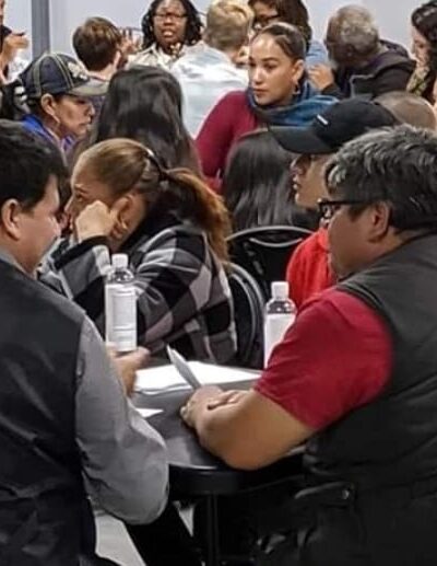 People attending a Campaign for Justice, Safety & Jobs event fill the room and are sitting around round tables.