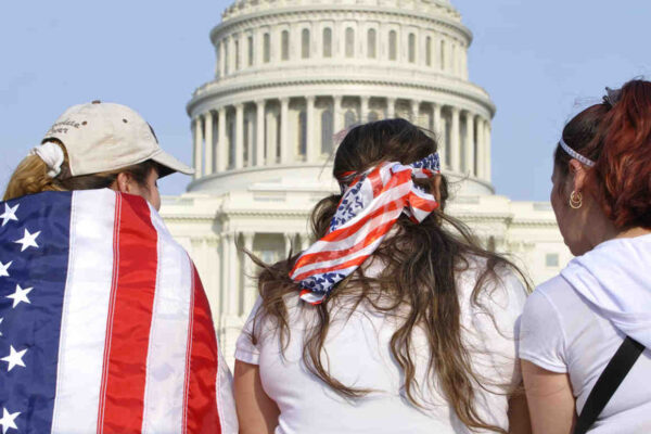 Three people are facing the US Capitol Building with American flags