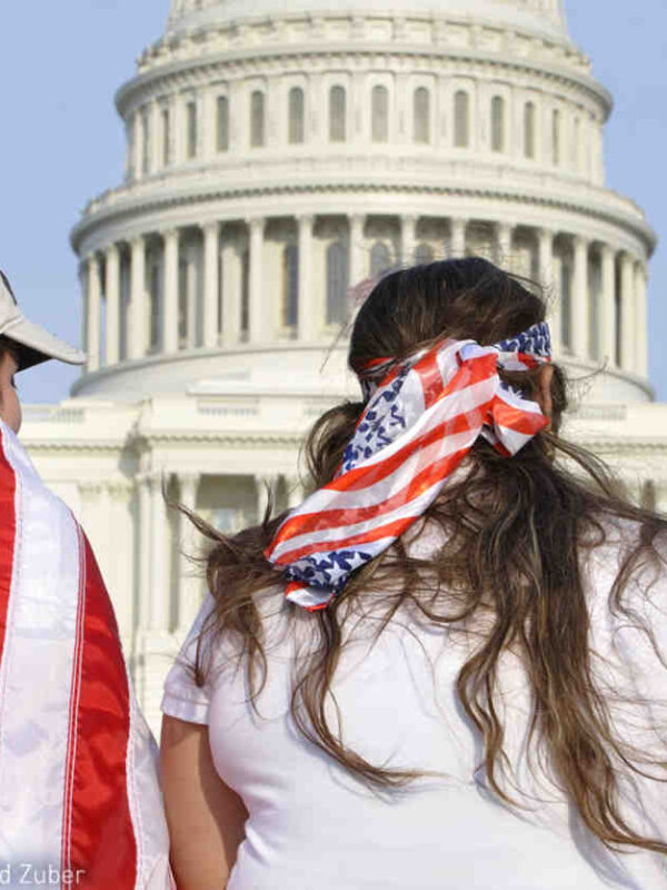 Three people are facing the US Capitol Building with American flags