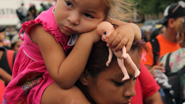 Immigrant family, child is sitting on parent's shoulders with a doll in her hands.