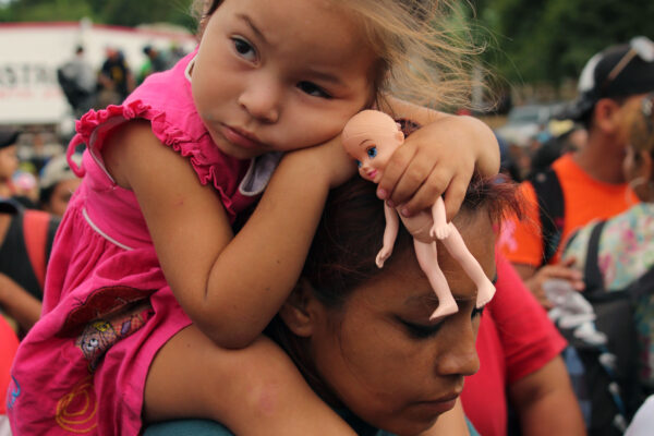 Immigrant family, child is sitting on parent's shoulders with a doll in her hands.