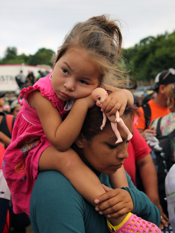 Immigrant family, child is sitting on parent's shoulders with a doll in her hands.