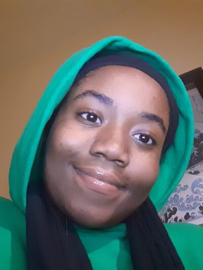 Queen Royalty is wearing a green hoodie with the hood up.