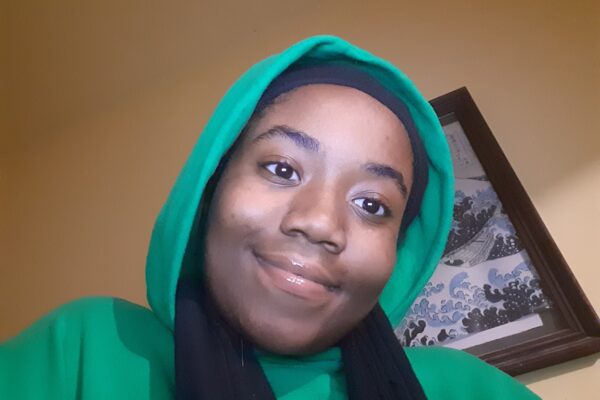 Queen Royalty is wearing a green hoodie with the hood up.