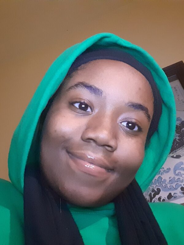 Queen Royalty is wearing a green hoodie with the hood up.