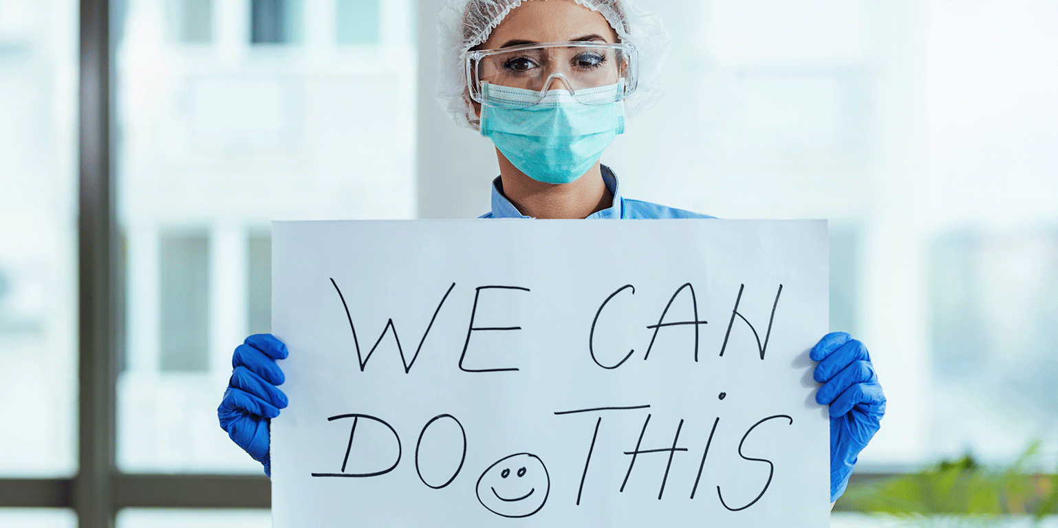 Healthcare worker in a mask and gloves holds a sign that says