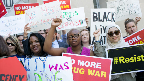 Protest with a Black person in the center with their fist raised. The signs say "no more drug war" and "Black Lives Matter" and "resist".