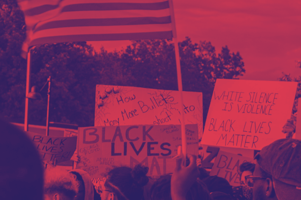 Image shows a protest for Black Lives Matter with a red and navy blue filter on it. People are holding a flag and protest signs.