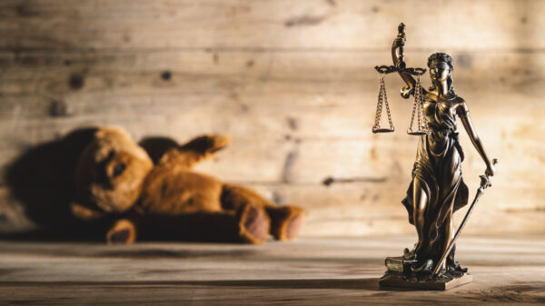Image shows justice scales and statue and a teddy bear laying on its side.