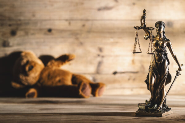 Image shows justice scales and statue and a teddy bear laying on its side.
