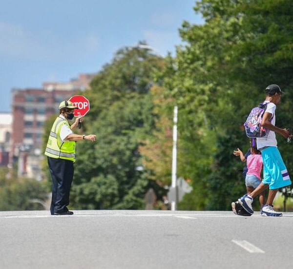 A crossing guard is guiding two students across a street.