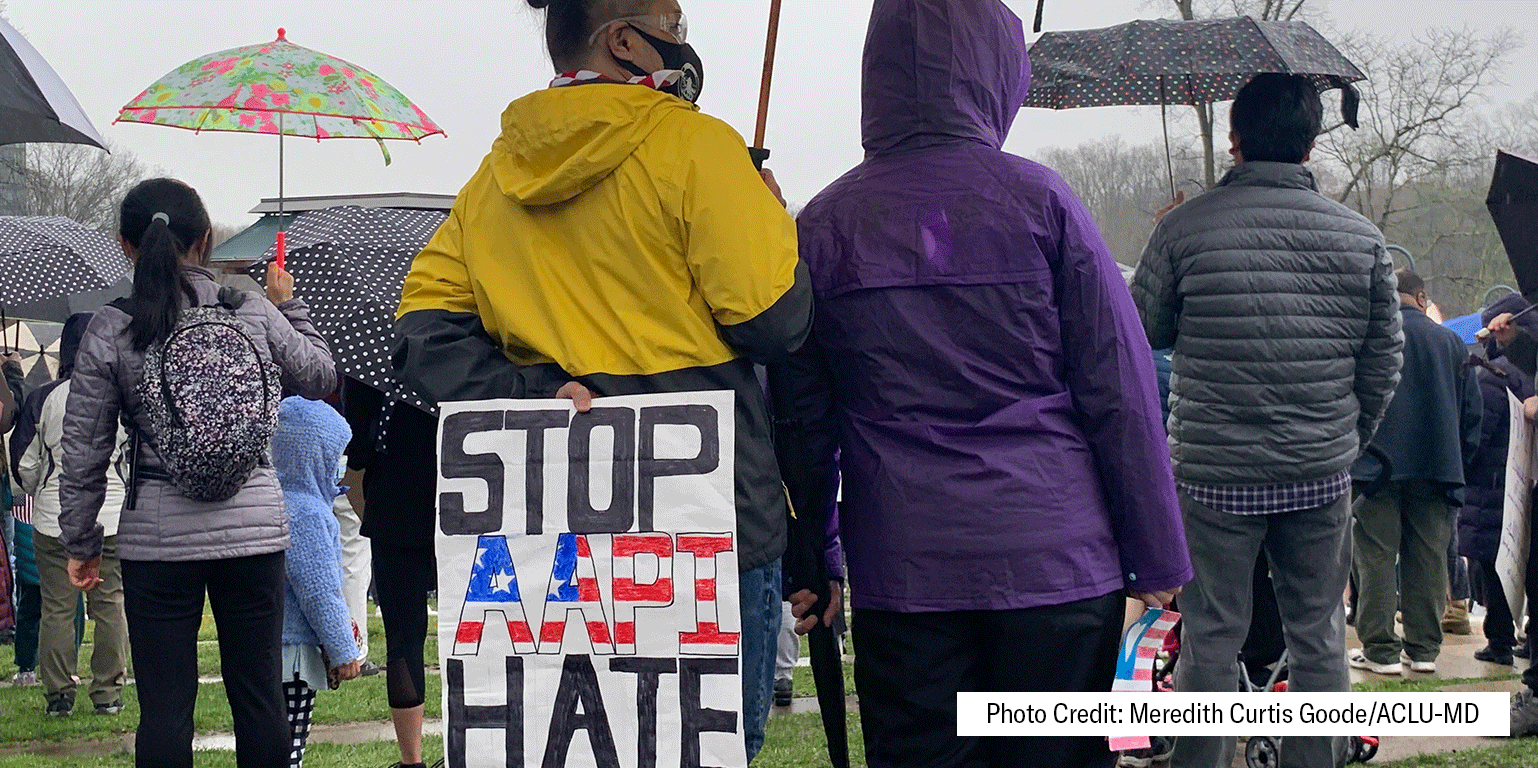 Person at a rally holds a sign behind their back that says,