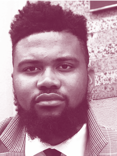Nehemiah Bester is a Black man with short hair and a beard, and is wearing a sport jacket, collared shirt, and tie. Image has a burgundy and white gradient map color profile.