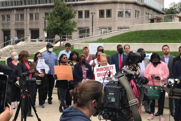 A group of activists stand outside together in Baltimore County at a press conference for the filing of a lawsuit to uphold the Voting Rights Act and create two majority-Black districts.