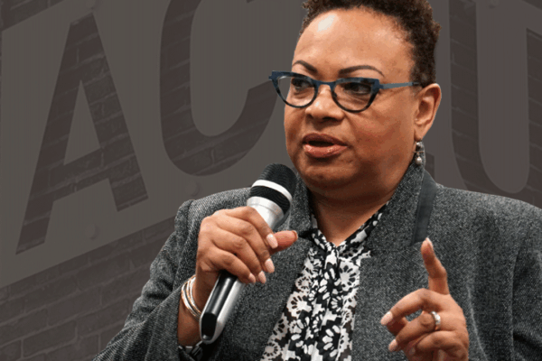 Dana Vickers Shelley is in the foreground and a picture of the ACLU sign and brick wall is in the background with a dark gray brown overlay.