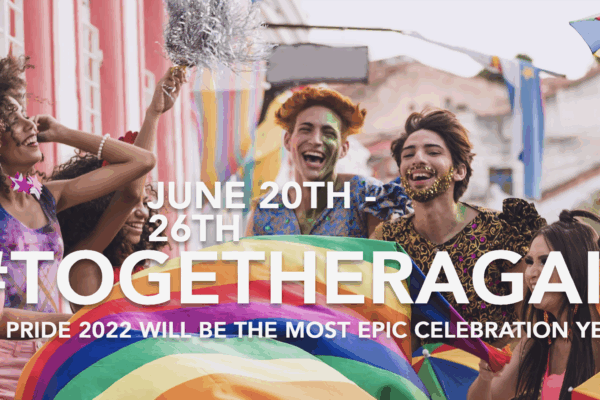 Group of people of various light to dark skin tones is laughing together holding a rainbow flag.