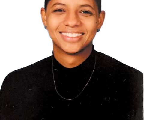 Aimy Avila is a Black-Latina woman with medium skin tone. She has her hair pulled back, is smiling at the camera, and is wearing a black mock-neck shirt. The background is all white.