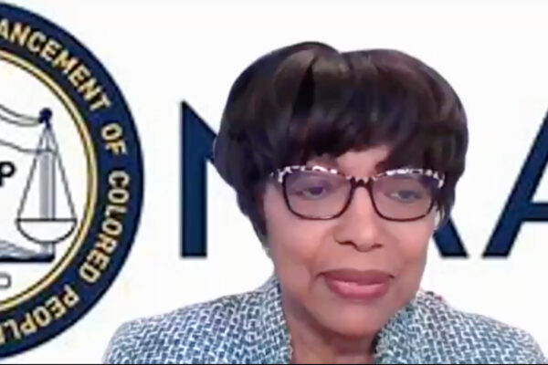 Dr. Willie Woods is a Black woman with medium brown skin. She has short dark hair, is wearing glasses, and is in front of a virtual background with part of the NAACP logo visible behind her.