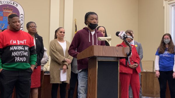 Press Conference:Group of mostly Black advocates are standing behind a podium. A young Black man is at the podium telling his story.