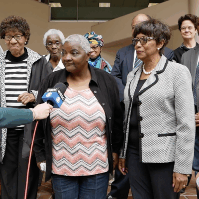 Group of plaintiffs and advocates from Federalsburg, Maryland, and lawyers from the ACLU of Maryland stand outside of a court buidling. A reporter is holding a microphone up to plaintiff Roberta Butler.