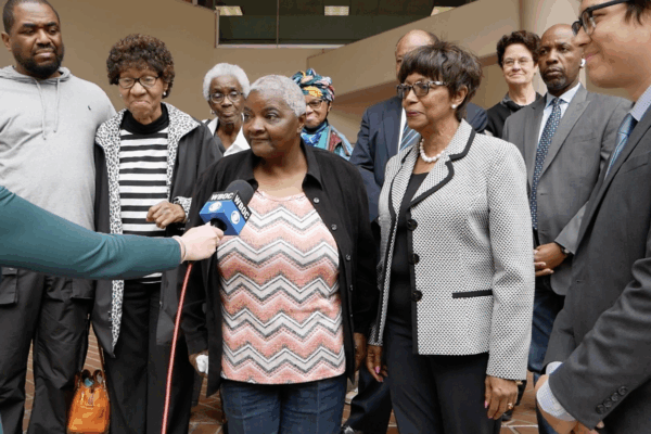 Group of plaintiffs and advocates from Federalsburg, Maryland, and lawyers from the ACLU of Maryland stand outside of a court buidling. A reporter is holding a microphone up to plaintiff Roberta Butler.