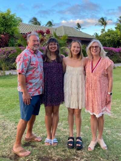 Olivia Spaccasi is standing with three family members. They are outside in Hawaii with trees, a house, and a blue sky behind them.