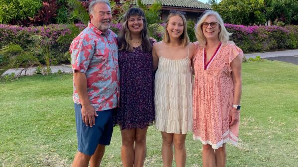 Olivia Spaccasi is standing with three family members. They are outside in Hawaii with trees, a house, and a blue sky behind them.