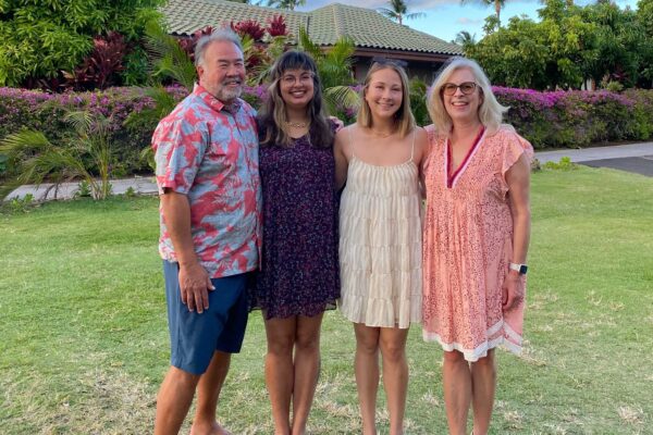 Olivia Spaccasi is standing with three family members. They are outside in Hawaii with trees, a house, and a blue sky behind them.