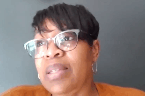 Josette Blocker is a Black woman with short hair swooped to the side. She is wearing cat-eye glasses and is looking toward the upper left of the screen.