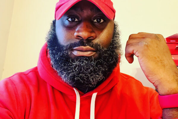 Ron Williams is a Black man wearing a red hat and hoodie, has a beard, and is looking at the camera. The text says, "End Police Stops and Searches Based on the Smell of Marijuana."