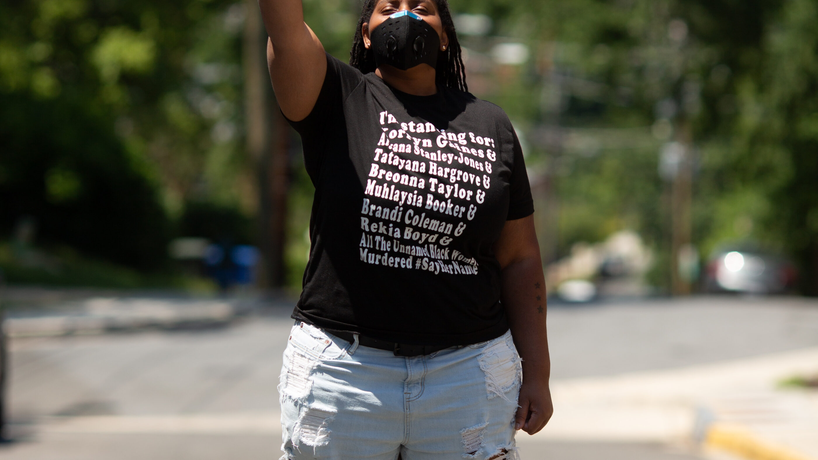 Black person with fist in the air wearing a t-shirt with the names of Black people killed by police