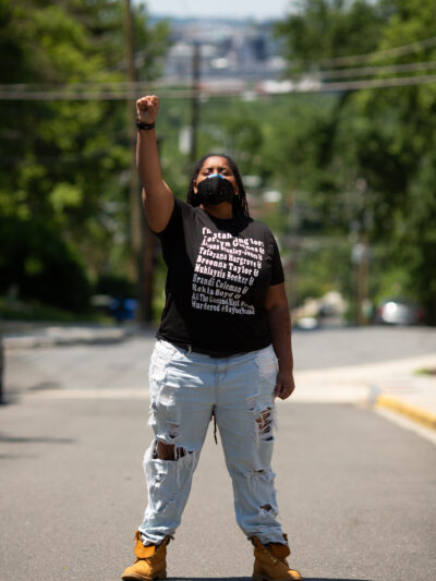 Black person with fist in the air wearing a t-shirt with the names of Black people killed by police