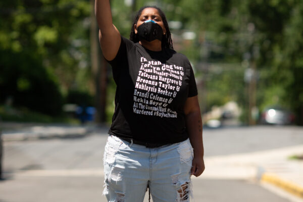 Black person with fist in the air wearing a t-shirt with the names of Black people killed by police