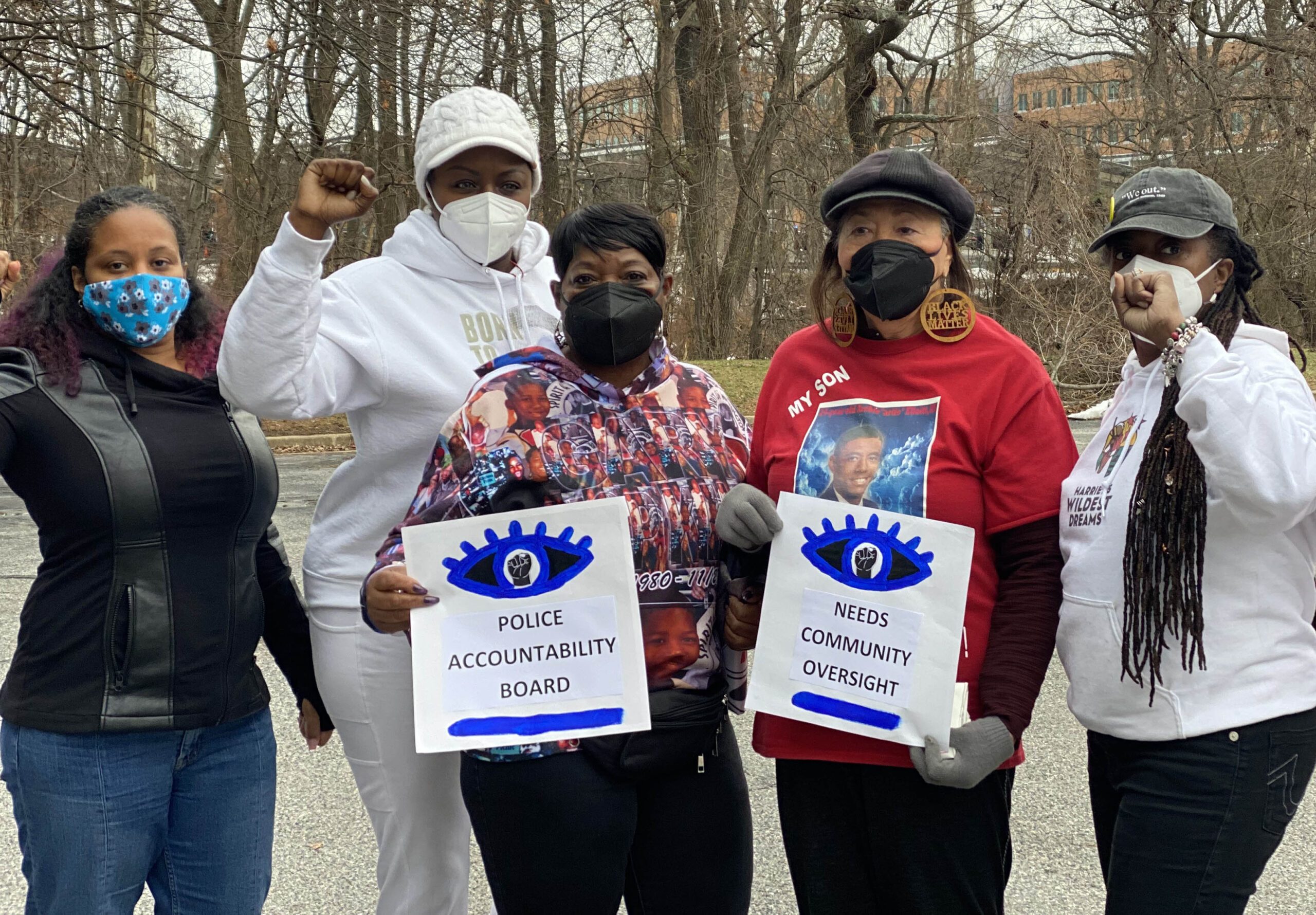 A group of Black and Residents of Color who are also advocates in Prince George's County are standing together. Two have their fists raised and two are holding signs that say "Police Accountability Board." Photo by Sergio España.
