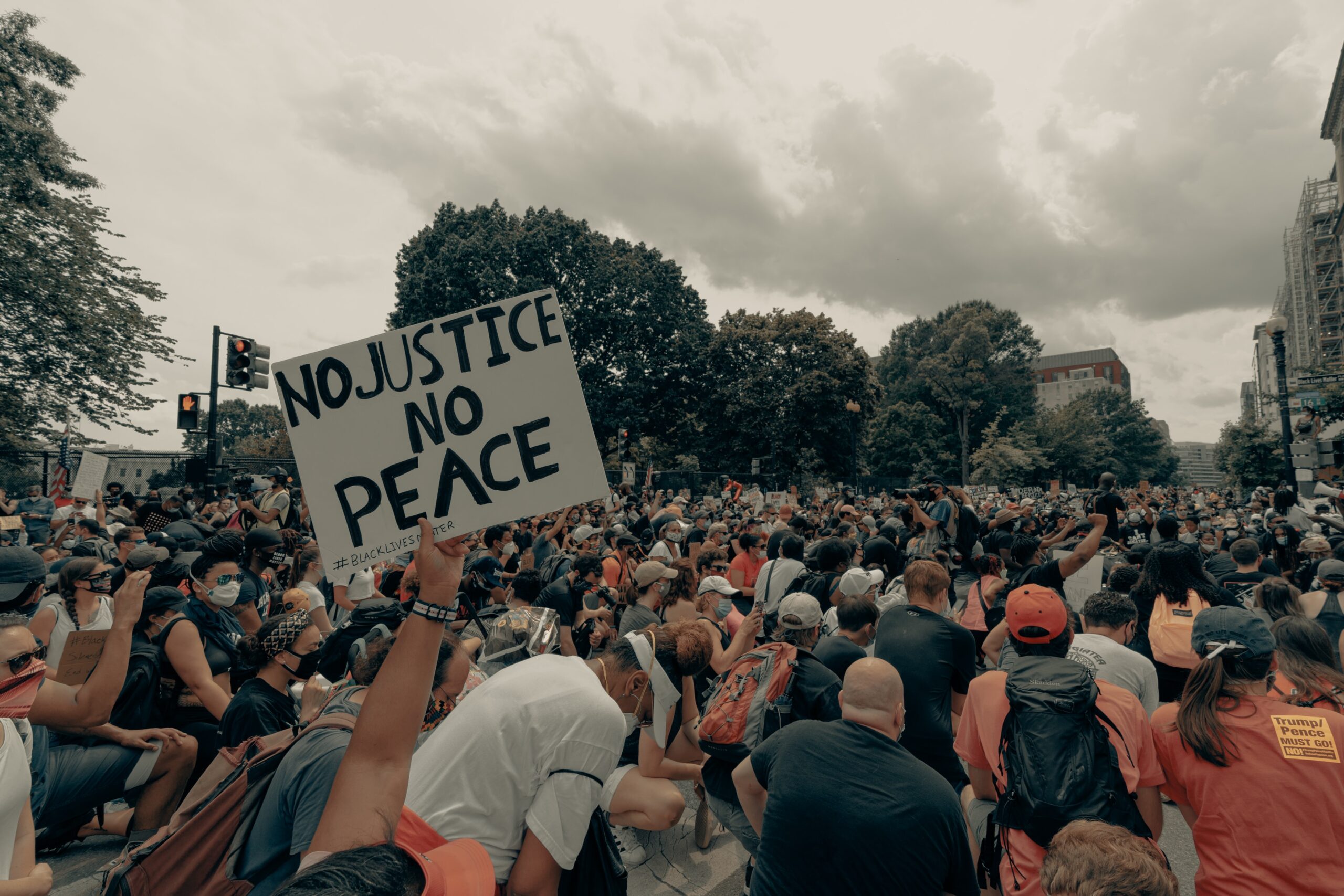 Group of people outside at a protest. Someone is holding a sign that says, "No Justice, No Peace."