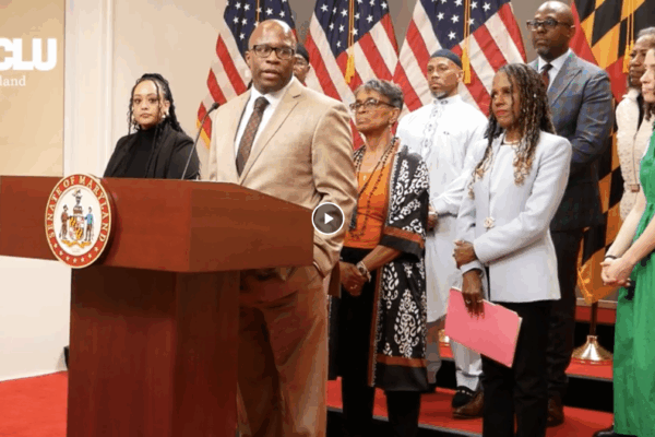 Anthony Muhammad is a Black man speaking at a podium at a press conference in Annapolis in support of the Maryland Second Look Act. There is a group of advocates standing behind him.