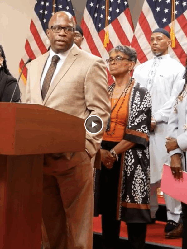 Anthony Muhammad is a Black man speaking at a podium at a press conference in Annapolis in support of the Maryland Second Look Act. There is a group of advocates standing behind him.