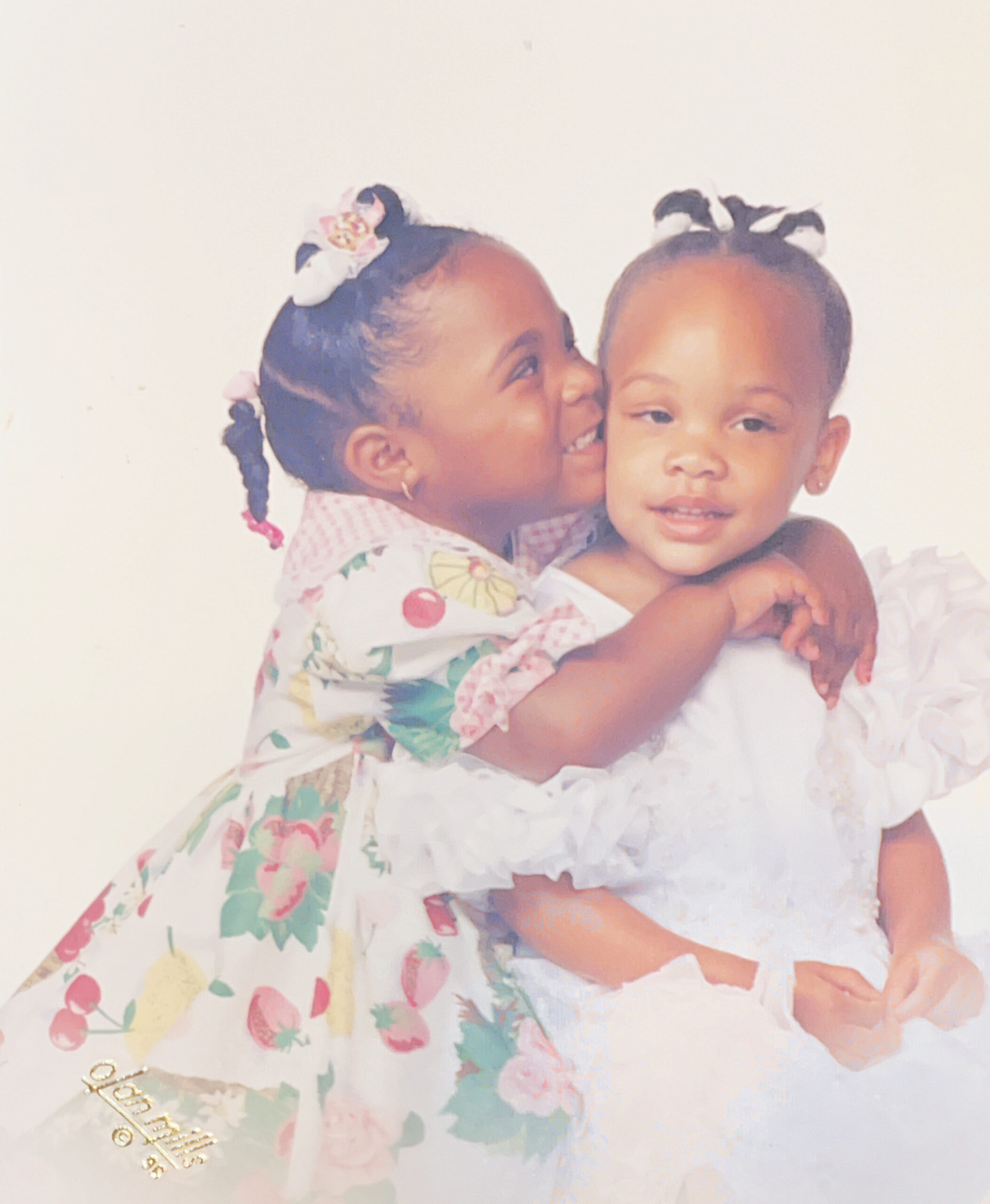 Antoinette and Alicia are sisters. They are young children in this photo of them hugging.They were at a very 90’s Olan Mills photoshoot.