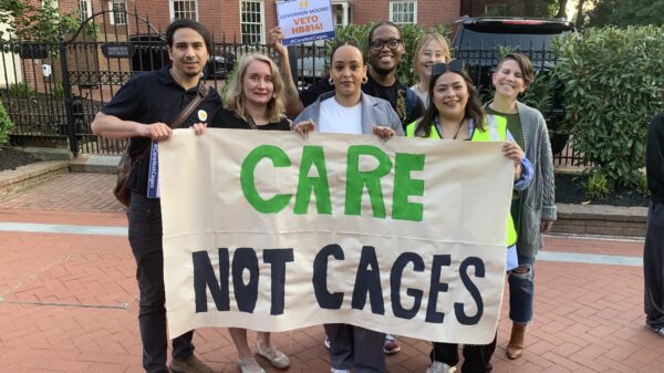ACLU of Maryland staff members hold a banner that says, "Care Not Cages." They are outside in Lawyer's Mall for a rally asking Governor Moore to veto HB 814.