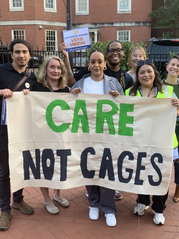 ACLU of Maryland staff members hold a banner that says, "Care Not Cages." They are outside in Lawyer's Mall for a rally asking Governor Moore to veto HB 814.