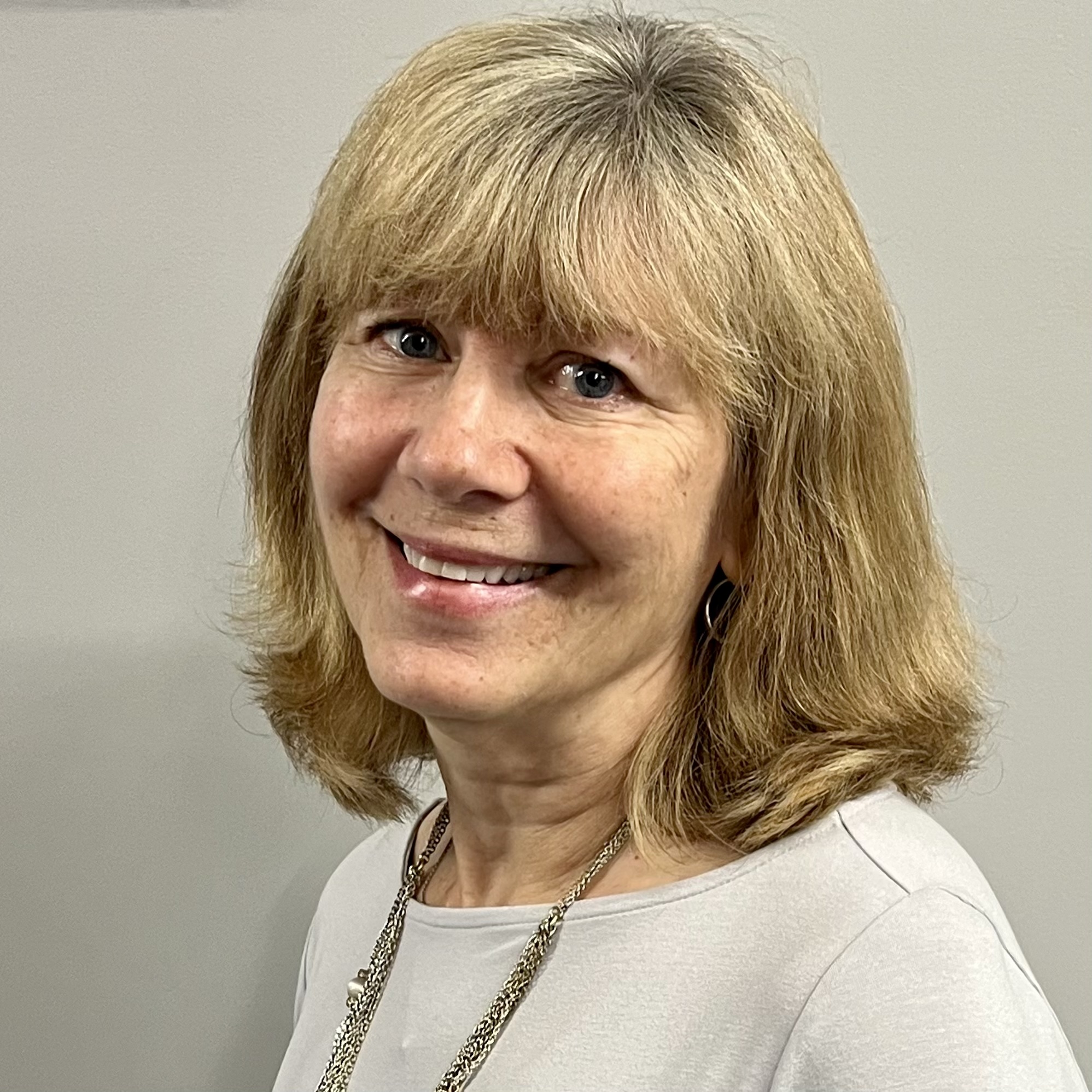 Val is a blonde woman seen smiling, wearing a necklace
